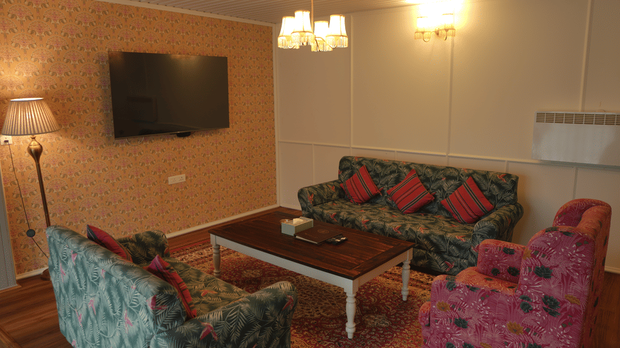 A living room at The Heritage Club Tripura Castle Hotel and Spa, Shillong featuring 3 sofas, a coffee table, a wall-mounted television, a floor lamp, and a chandelier.