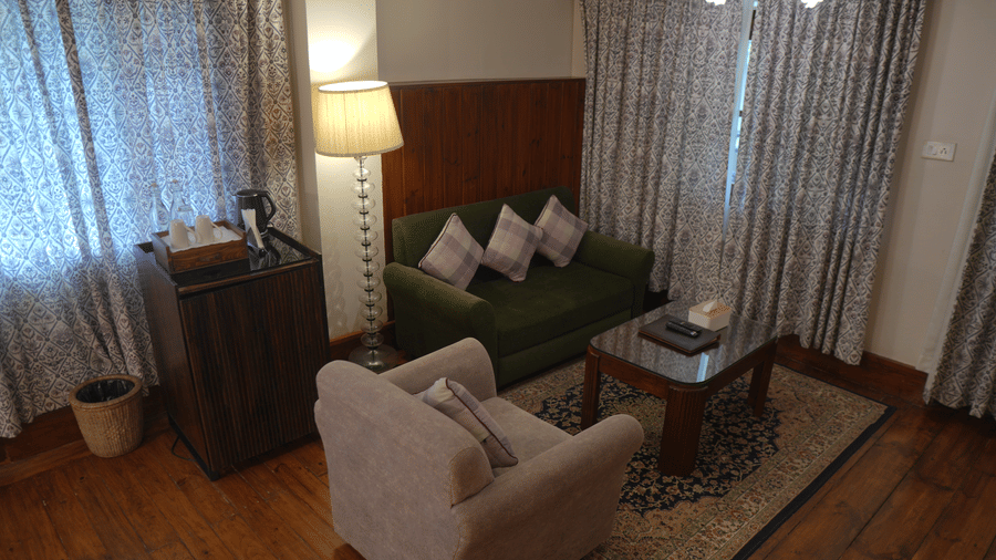 A sitting area at The Heritage Club Tripura Castle Hotel and Spa, Shillong featuring a sofa, an armchair, a coffee table, a floor lamp, and a mini fridge setup.