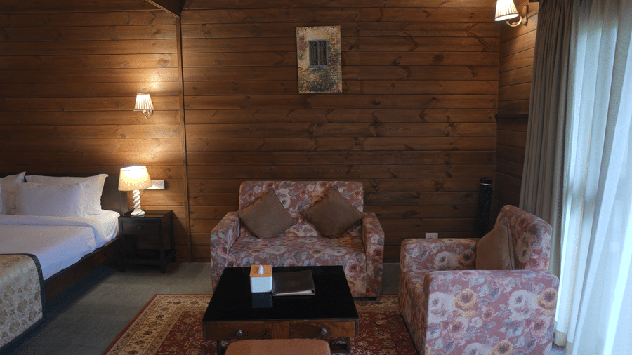 A sitting area at The Heritage Club Tripura Castle Hotel and Spa, Shillong featuring a sofa, an armchair, a coffee table, a rug, and wood panelled walls.  