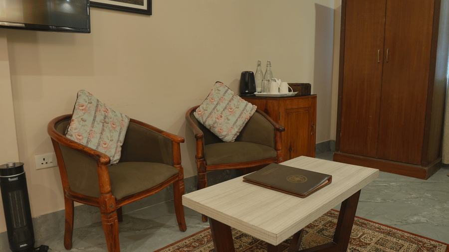 A sitting area at The Heritage Club Tripura Castle Hotel and Spa, Shillong featuring 2 armchairs, a coffee table, a tea set, and a wardrobe.  