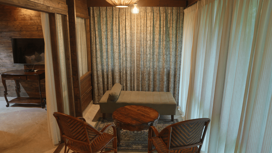 A sitting area at The Heritage Club Tripura Castle Hotel and Spa, Shillong featuring a daybed, 2 chairs, a coffee table, and curtained windows.  