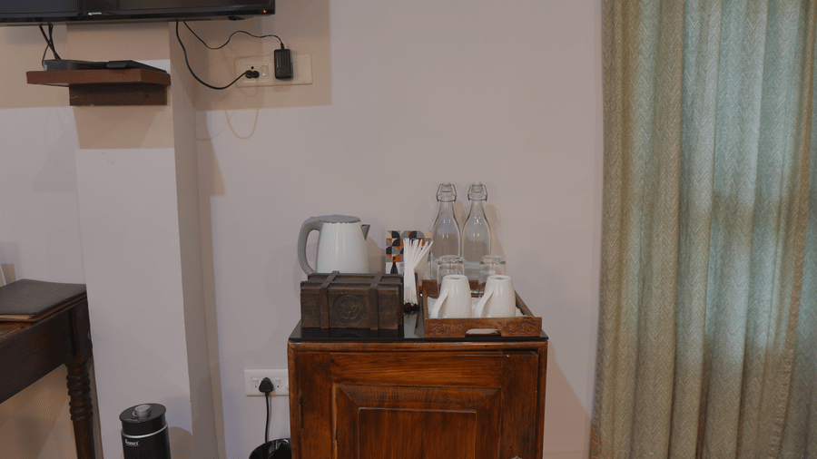 A tea station at The Heritage Club Tripura Castle Hotel and Spa, Shillong featuring an electric kettle, water bottles, teacups, and a wooden cabinet.  