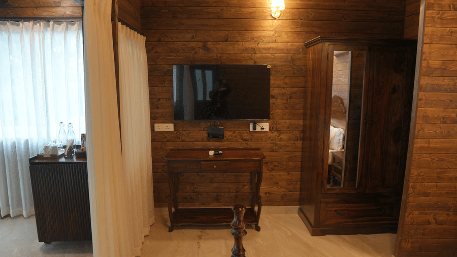 A room with wall mounted television, wooden wardrobe, and desk unit at The Heritage Club Tripura Castle Hotel and Spa, Shillong.