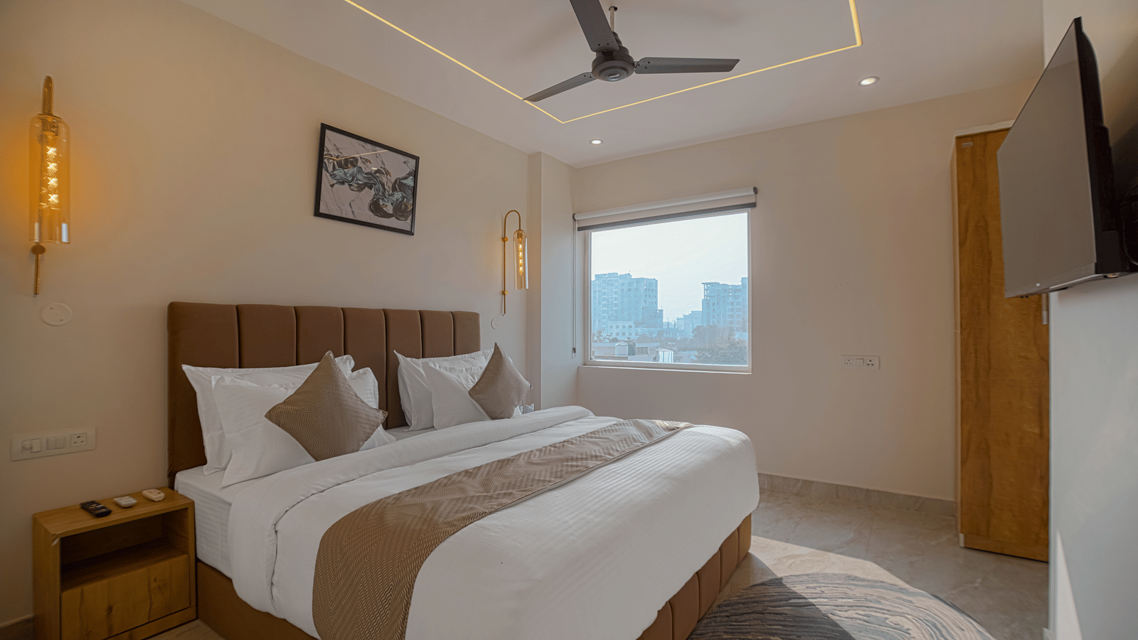 A contemporary room at Perfectstayz Premium Varanasi with a king size bed, beige and brown theme, a wall-mounted TV, and a window overlooking the city.