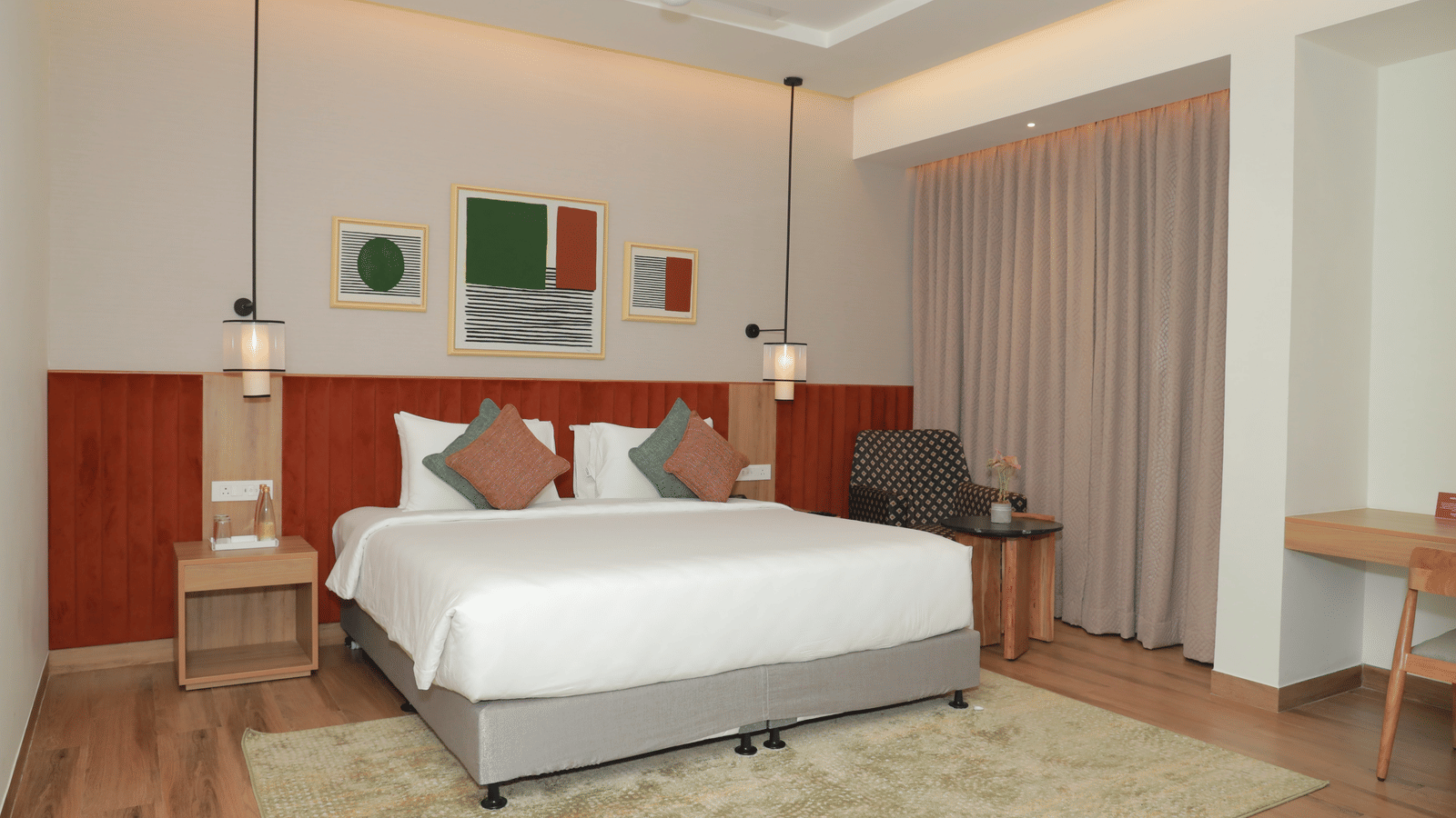 A suite with a large bed, a bed bench, and an upholstered chair in one of our hotel rooms in Tuticorin - Regency Tuticorin by GRT Hotels