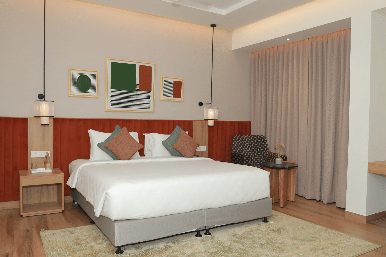 A suite with a large bed, a bed bench, and an upholstered chair in one of our hotel rooms in Tuticorin - Regency Tuticorin by GRT Hotels