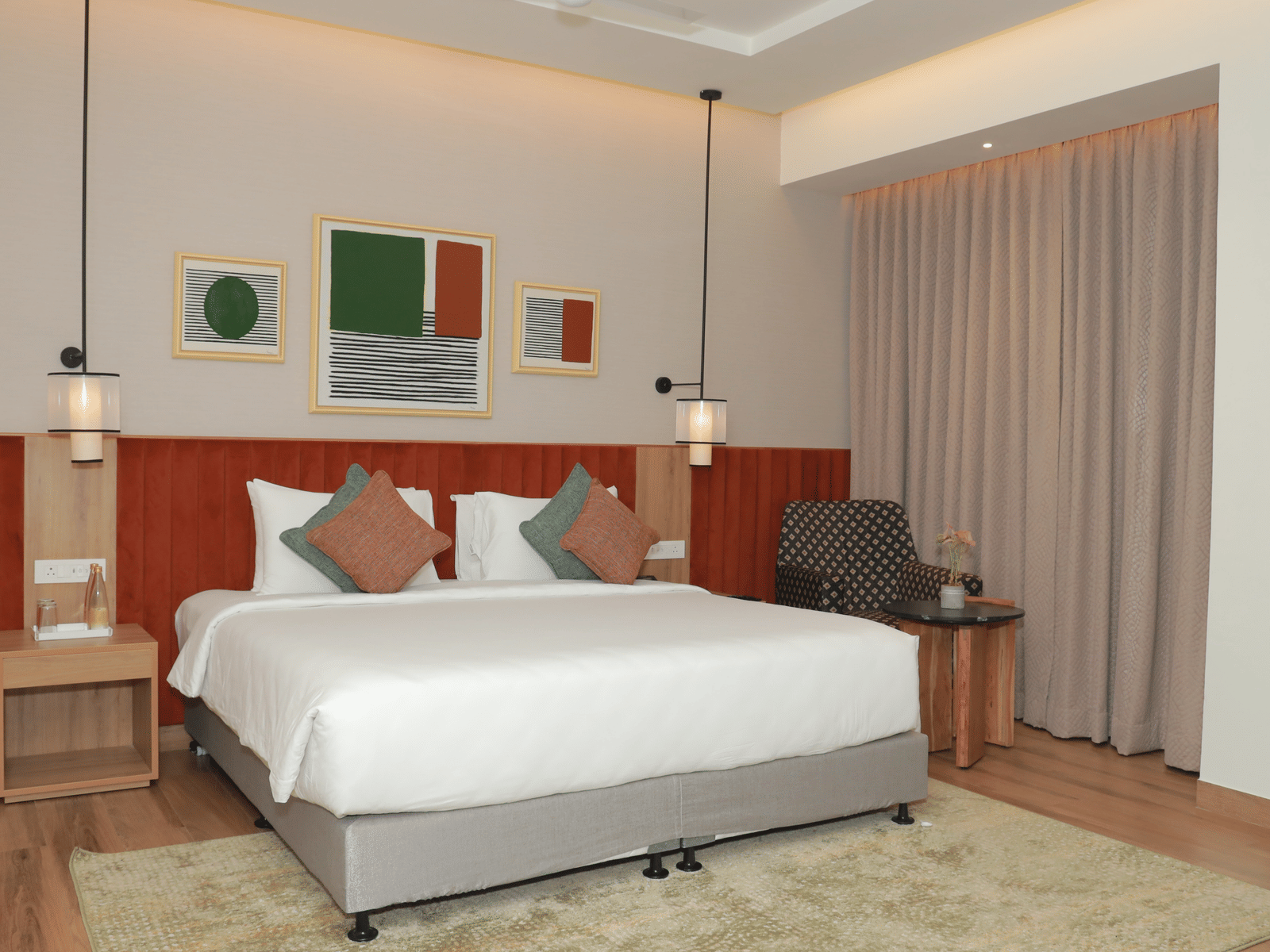 A suite with a large bed, a bed bench, and an upholstered chair in one of our hotel rooms in Tuticorin - Regency Tuticorin by GRT Hotels