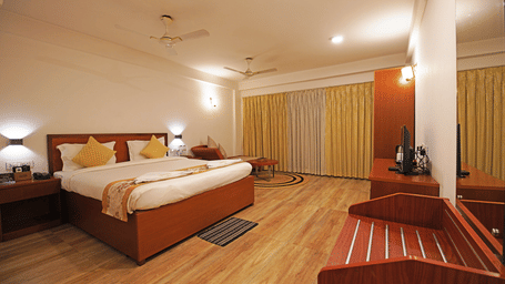 Executive Room at Hotel Sonar Bangla, Kolaghat, featuring a room with warm lighting, a plush double bed, wooden flooring, and closed curtains.