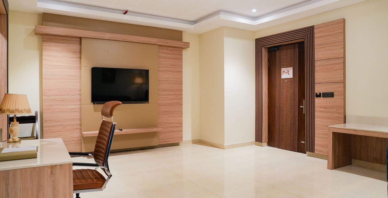 A contemporary living space of the Empress Suite at The Meriton, showing a large wall-mounted television, a wooden media console, and a work desk.