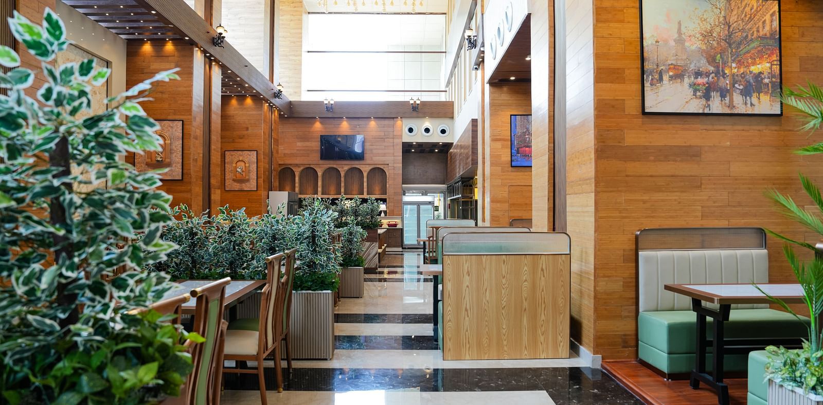 A bright and inviting dining area at The Meriton, adorned with lush green plants, comfortable booth seating in light green, and wooden wall accents.