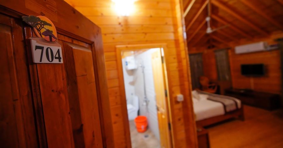 Door opening to the Wooden House of GK Hill View Resort furnished with ample lighting, wooden architecture, wall-mounted TV and more.