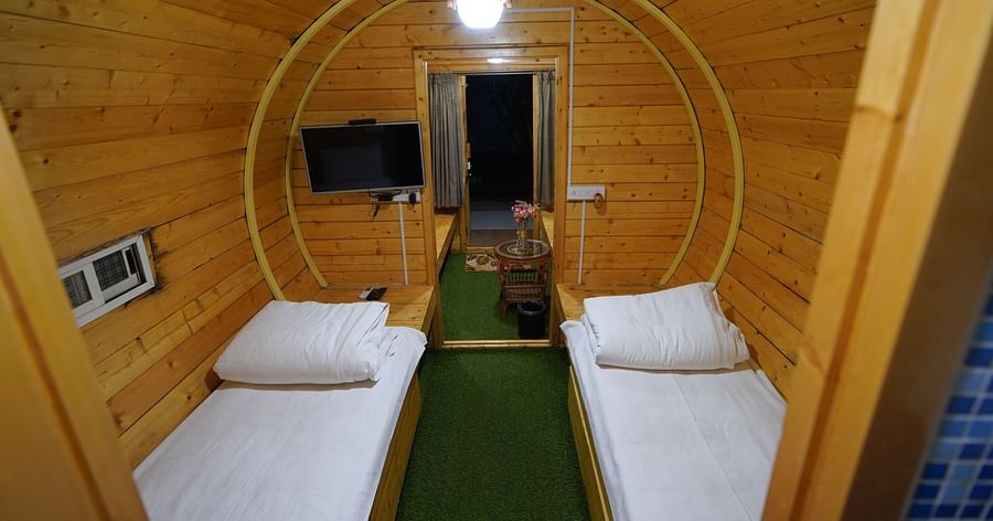 Interior of the round-shaped Wooden House at GK Hill View Resort furnished with twin beds, shelves, seating area, wall-mounted TV and overhead lighting.