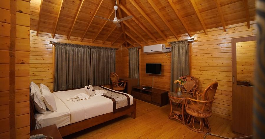Wooden House of GK Hill View Resort furnished with double bed, sitting chairs, wall-mounted TV, curtained windows and lighting.