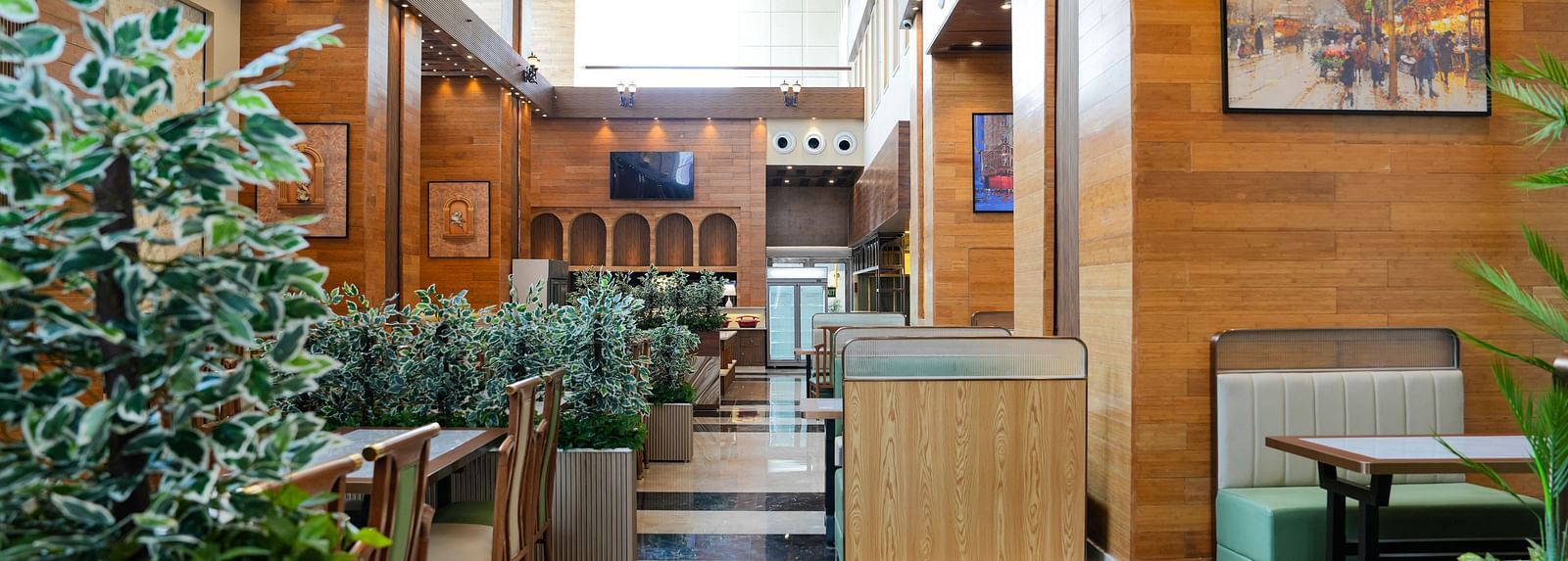 A bright and inviting dining area at The Meriton, adorned with lush green plants, comfortable booth seating in light green, and wooden wall accents.