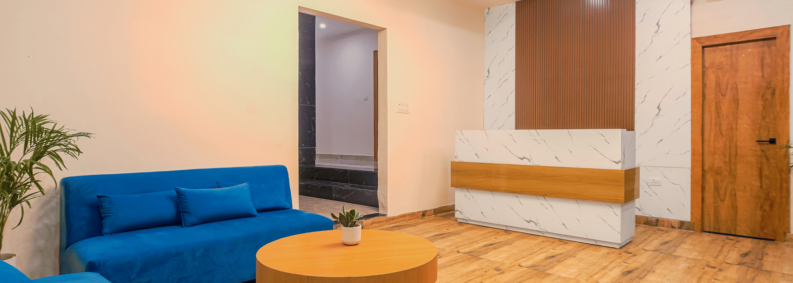 A contemporary hotel lounge featuring a bright blue sofa and a round wooden table in a well-lit room at Perfectstayz Premium Varanasi.