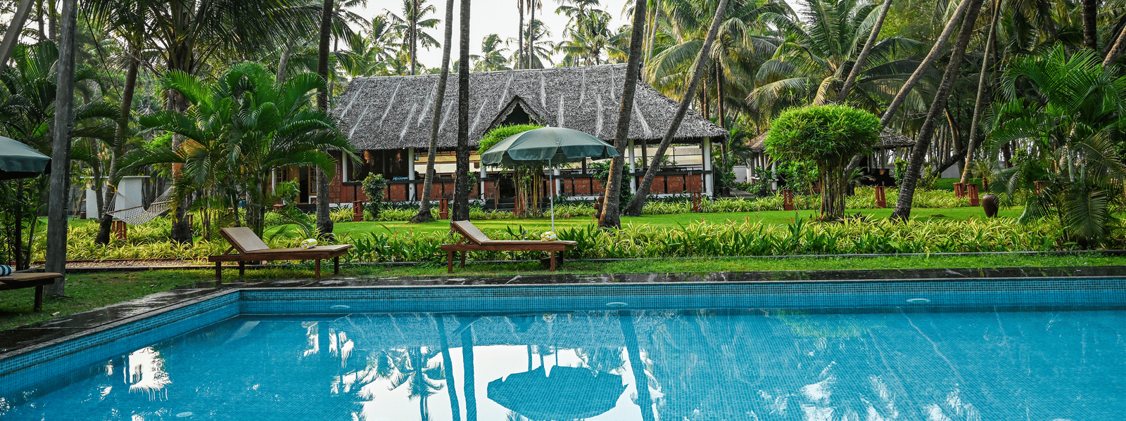 The outdoor swimming pool surrounded by tropical palm trees and greenery at Ayur On The Beach Nattika.