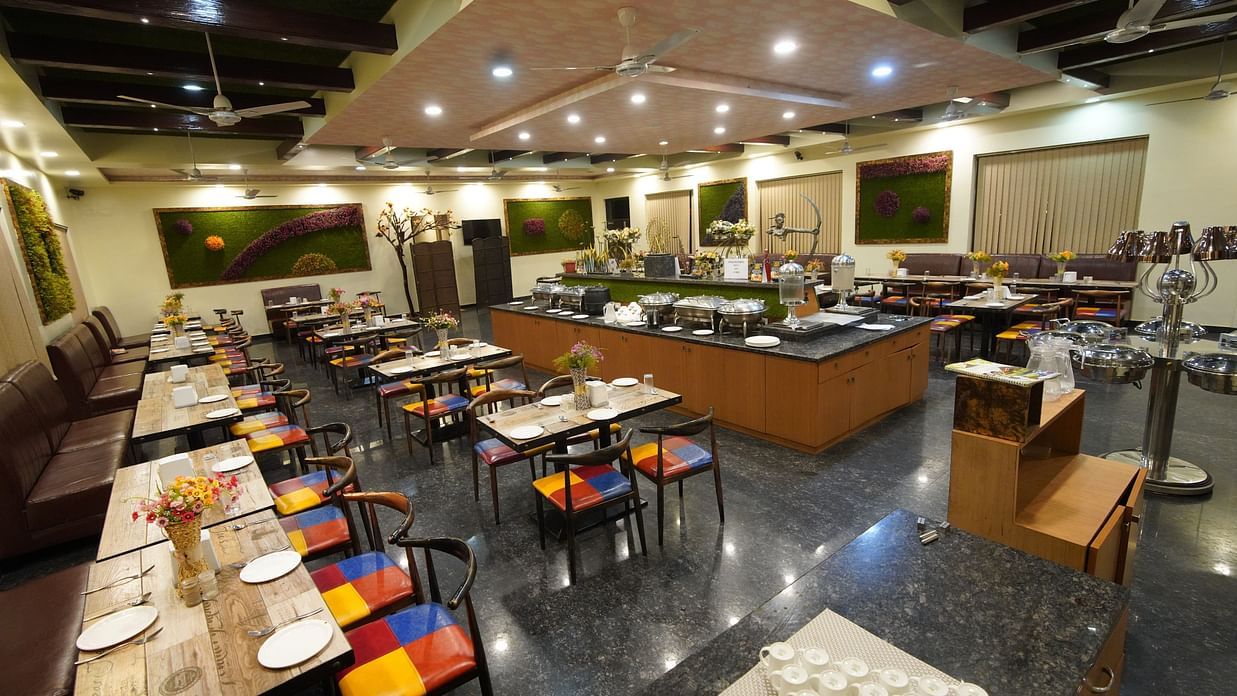 In-house restaurant of GK Hill View Resort with parallel aligned tables, overhead lighting.