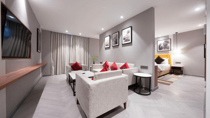 Well-appointed twin room at The HHI Varanasi featuring two beds with yellow headboard and crisp white bedding with dark accent pillows and bedside lamps alongside a work desk and wall-mounted TV.