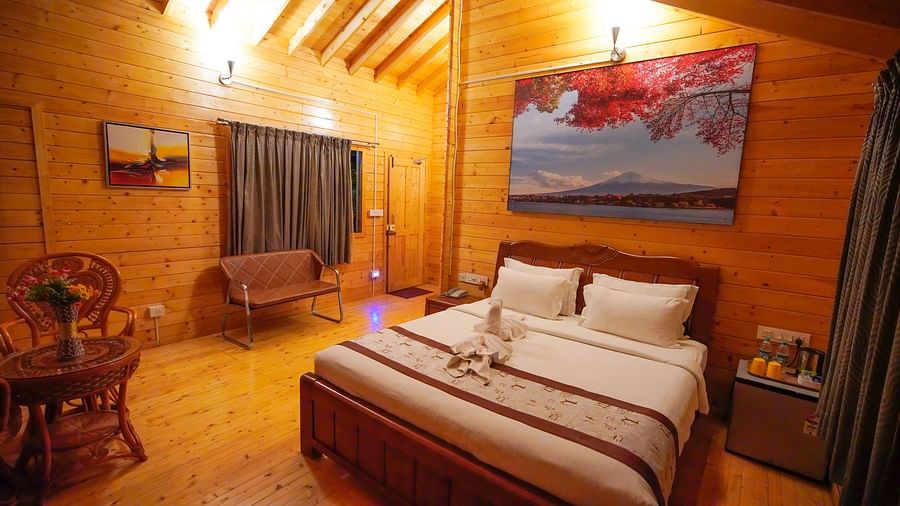 Wooden House of GK Hill View Resort furnished with double bed, sitting chairs, wall-mounted TV, curtained windows and lighting.
