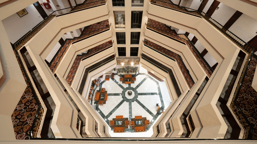 A downward view from an upper floor into an octagonal lobby area with seating and tables | HHI Varanasi