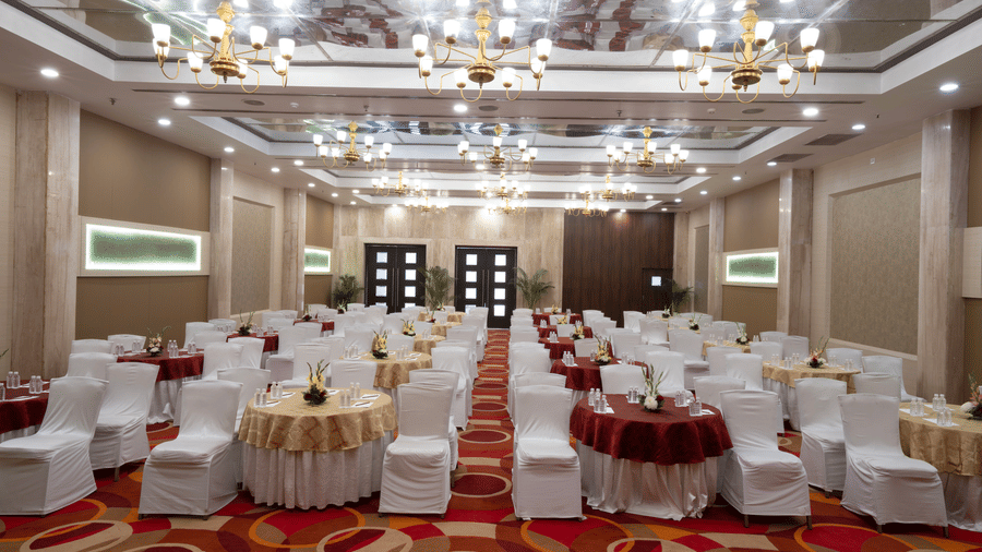 An interior view of a function hall with round tables and chairs with white covers | HHI Varanasi
