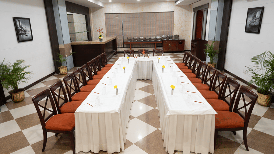 A meeting room with white-clothed tables arranged in a U-shape and wooden chairs with red seats | HHI Varanasi