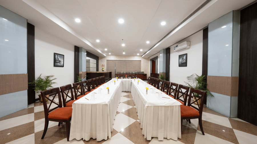 A long meeting room with two rows of tables covered in white cloths and wooden chairs with red cushions | HHI Varanasi