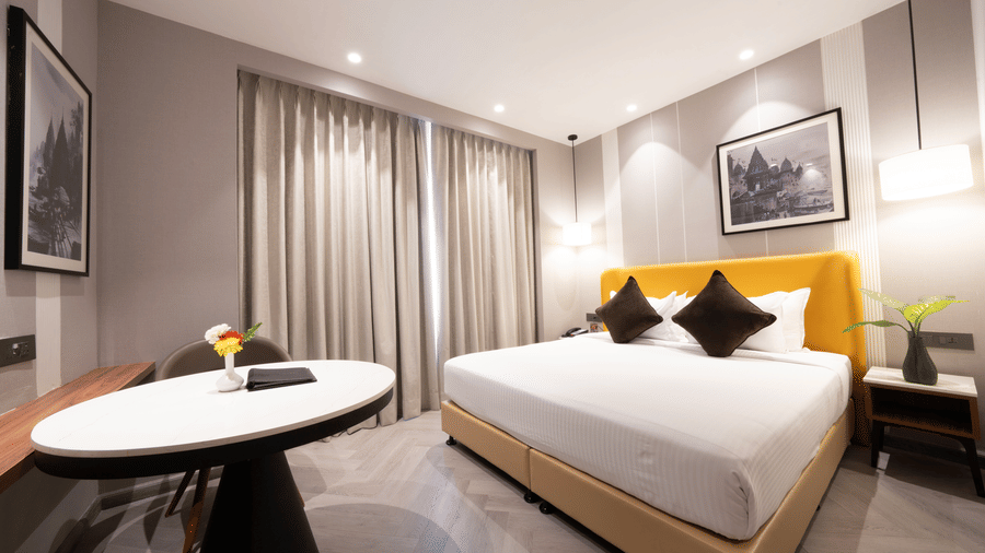 A hotel room with a double bed, a white oval table, and grey curtains | HHI Varanasi