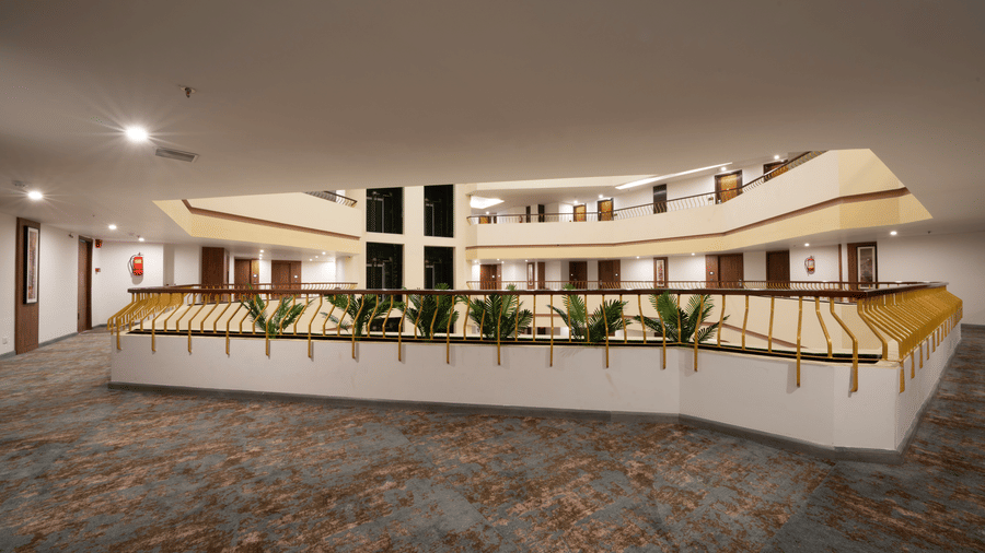 Multi-level hotel atrium corridor with gold railings, indoor palms, carpeted floors, and room balconies.
