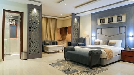 A wide view of the Premium Room at The Meriton, combining a sleeping area with a large king size bed and an adjoining sitting area with a chaise lounge.