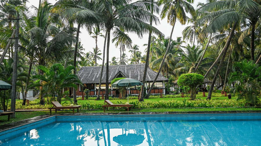 The outdoor swimming pool surrounded by tropical palm trees and greenery at Ayur On The Beach Nattika.
