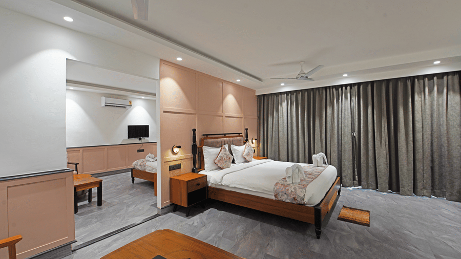 Corner view of one of the rooms in the Suite Quad of Hotel Sonar Bangla, Kolaghat, featuring well-lit interiors, a plush double bed, and a partition with an entry on one side offering access to the other room.