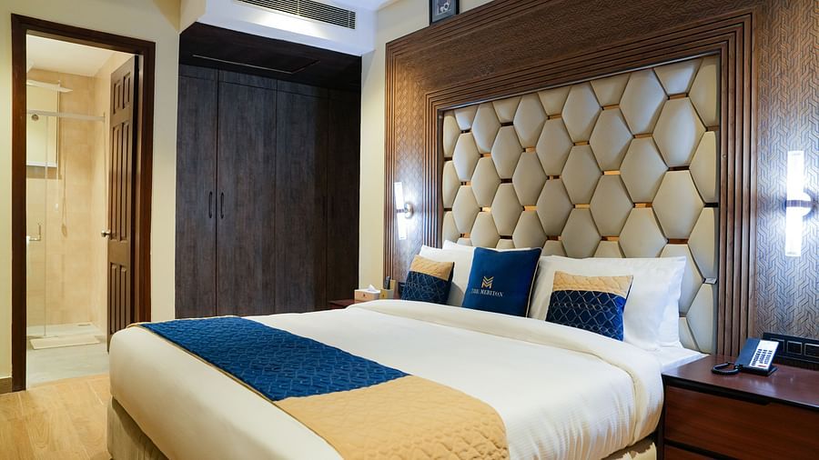 A well-appointed double bedroom at The Meriton, featuring a large bed with a padded headboard, crisp white and blue bedding, and a bedside table with a lamp at the Empress Suite.