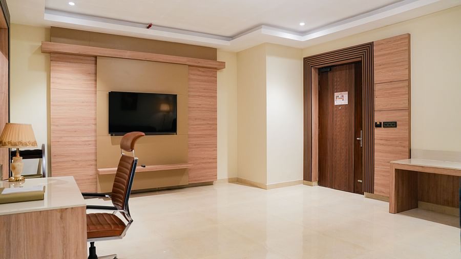 A contemporary living space of the Empress Suite at The Meriton, showing a large wall-mounted television, a wooden media console, and a work desk.