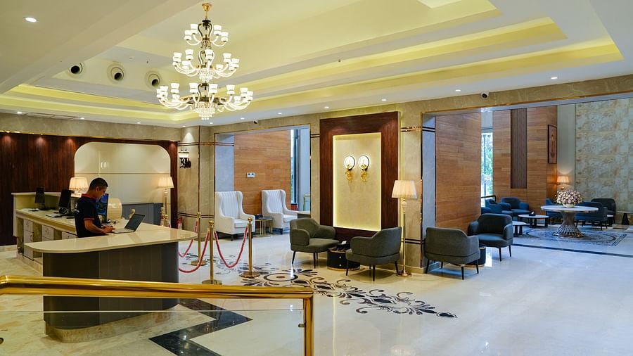A grand and spacious lobby area at The Meriton, showcasing elegant chandeliers, comfortable seating, and reflective marble flooring.
