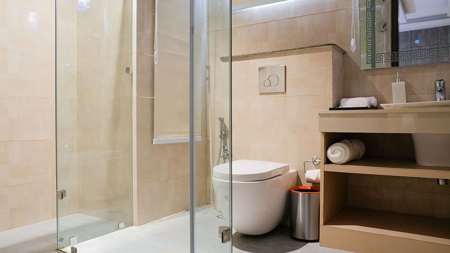 A clean and modern bathroom at The Meriton, featuring a glass-enclosed shower cubicle, a commode, and integrated shelving with toiletries, all in neutral tones.