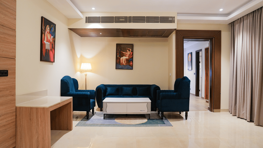 A comfortable and stylish living area at the Empress Suite at The Meriton, furnished with a deep blue sofa, a coffee table, and an accent chair | Accommodation in New Delhi