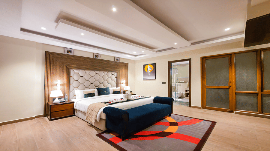 A well-appointed double bed accommodation in New Delhi at The Meriton, featuring a large bed with a padded headboard, crisp white and blue bedding, and a bedside table with a lamp at the Empress Suite.