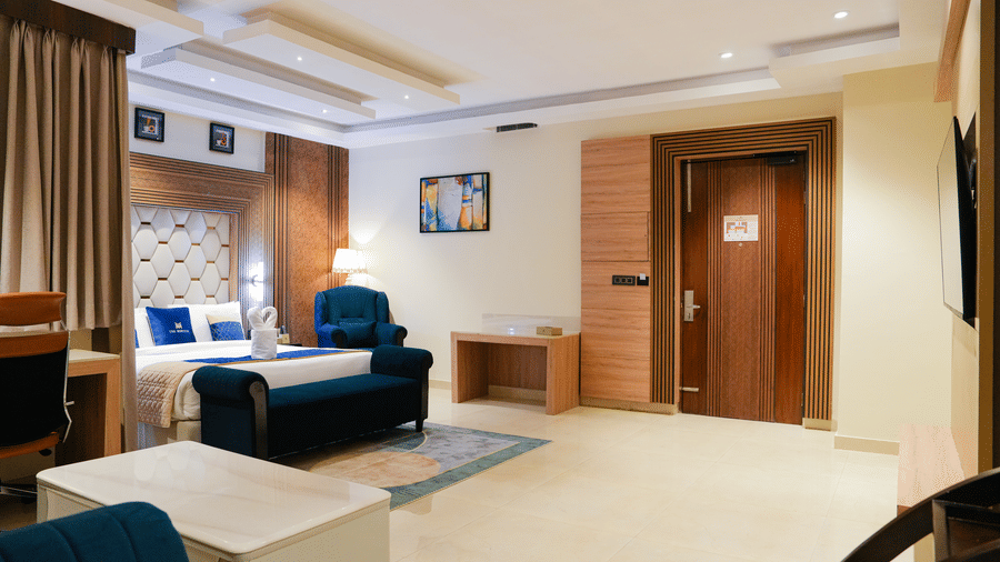 A welcoming living area at the Presidential Suite in Delhi at The Meriton, showing a comfortable sofa, a patterned rug, and a glimpse of an adjoining bedroom or entrance.