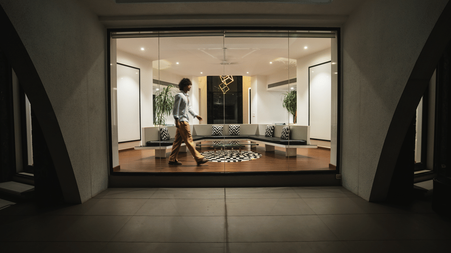 View from a dark concrete tunnel entryway looking out into a brightly lit, modern luxury living room with a person walking inside.