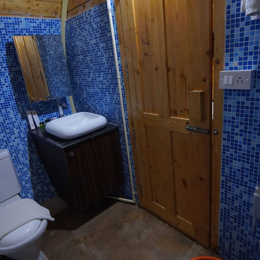 Bathroom of the round-shaped Wooden House at GK Hill View Resort furnished with a western commode, turkey towel, sink and a door.