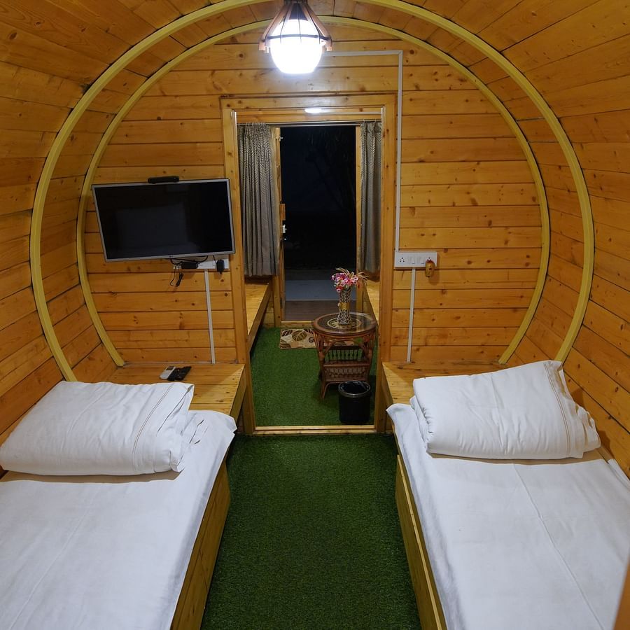 Interior of the round-shaped Wooden House at GK Hill View Resort furnished with twin beds, shelves, seating area, wall-mounted TV and overhead lighting.