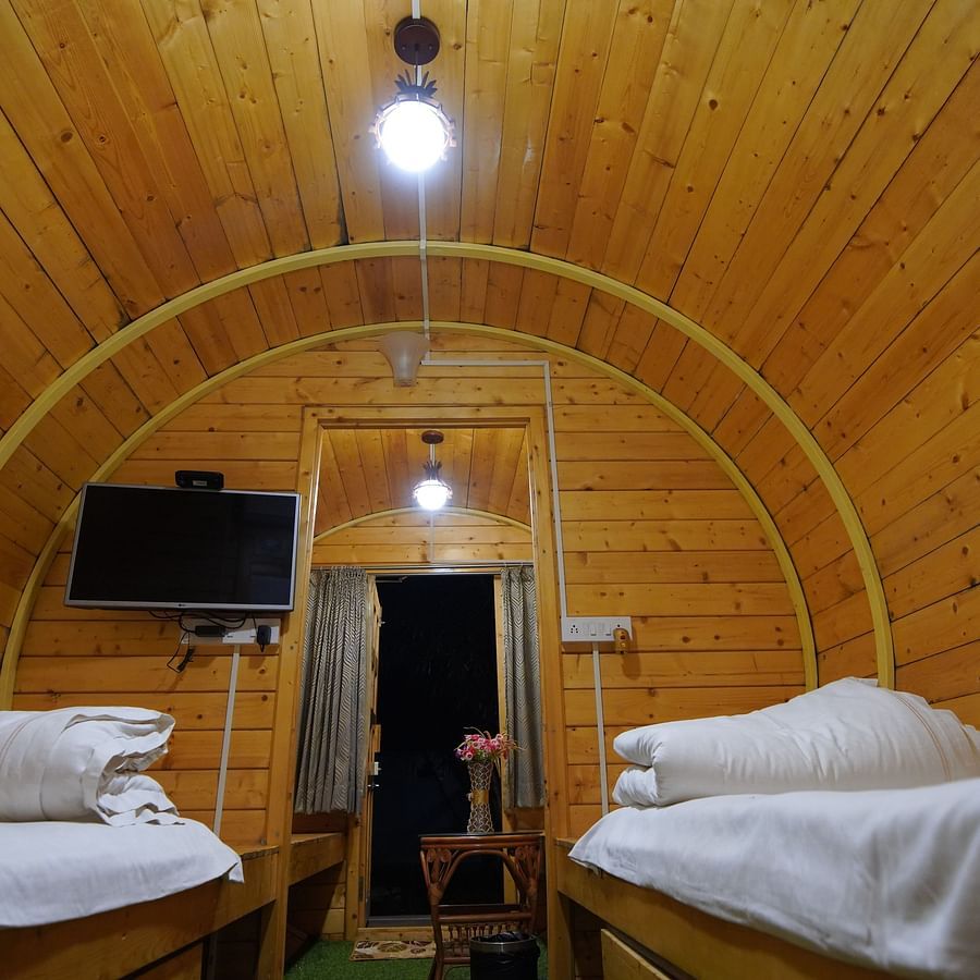 Interior of the round-shaped Wooden House at GK Hill View Resort furnished with twin beds, shelves, seating area, wall-mounted TV and overhead lighting.