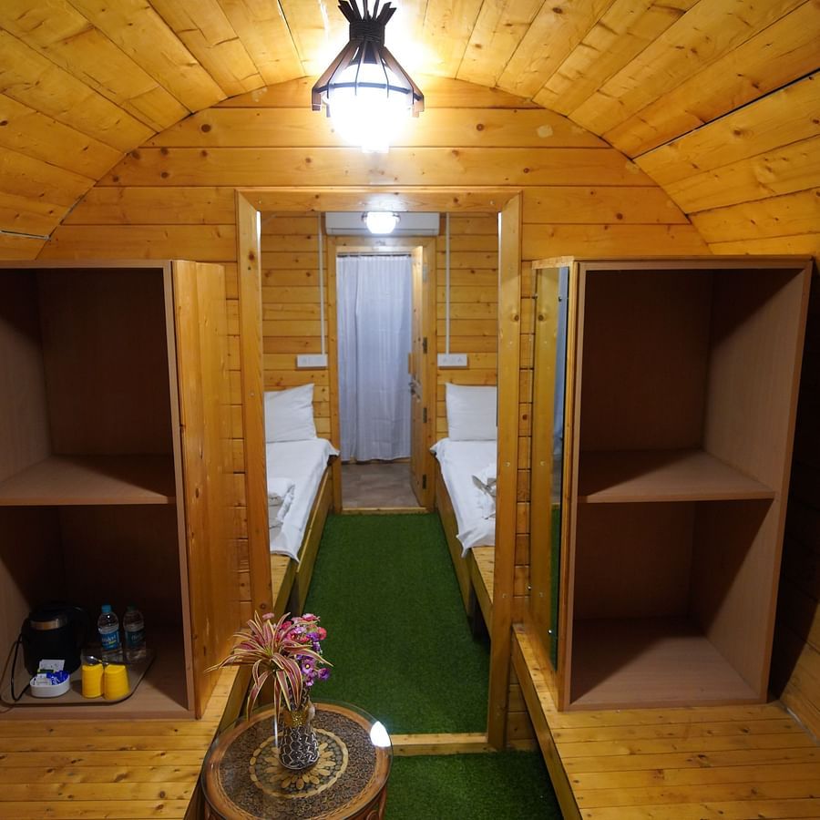 Interior of the round-shaped Wooden House at GK Hill View Resort furnished with twin beds, shelves, seating area and overhead lighting.