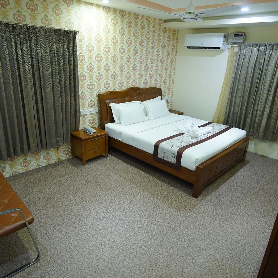 Themed Villas of GK Hill View Resort furnished with a double bed, wall-mounted AC, a chair and curtained windows.
