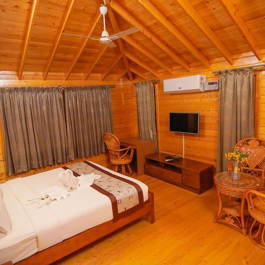 Wooden House of GK Hill View Resort furnished with double bed, sitting chairs, wall-mounted TV, curtained windows and lighting.