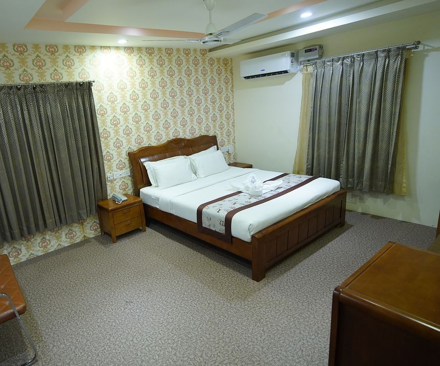 Themed Villas of GK Hill View Resort furnished with a double bed, wall-mounted AC, a chair and curtained windows.