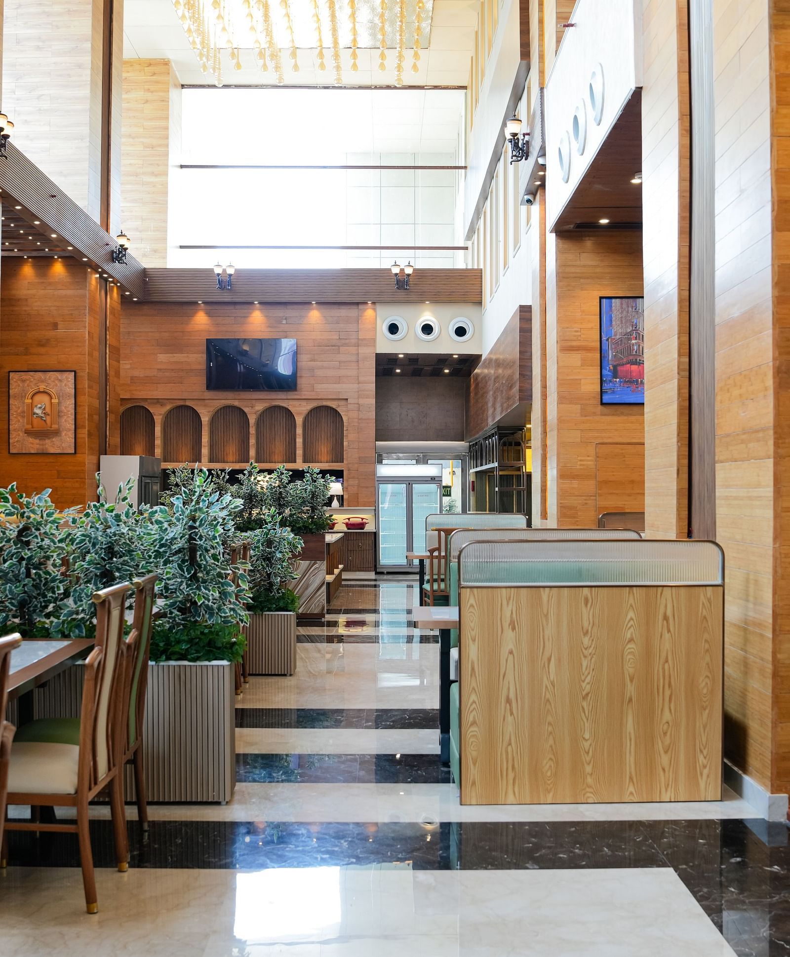 A bright and inviting dining area at The Meriton, adorned with lush green plants, comfortable booth seating in light green, and wooden wall accents.