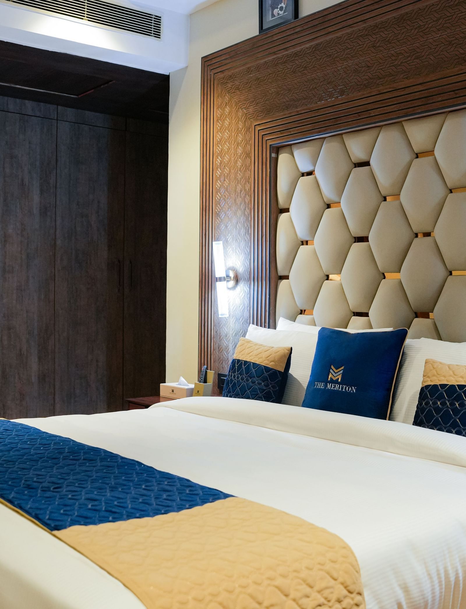 A well-appointed double bedroom at The Meriton, featuring a large bed with a padded headboard, crisp white and blue bedding, and a bedside table with a lamp at the Empress Suite.