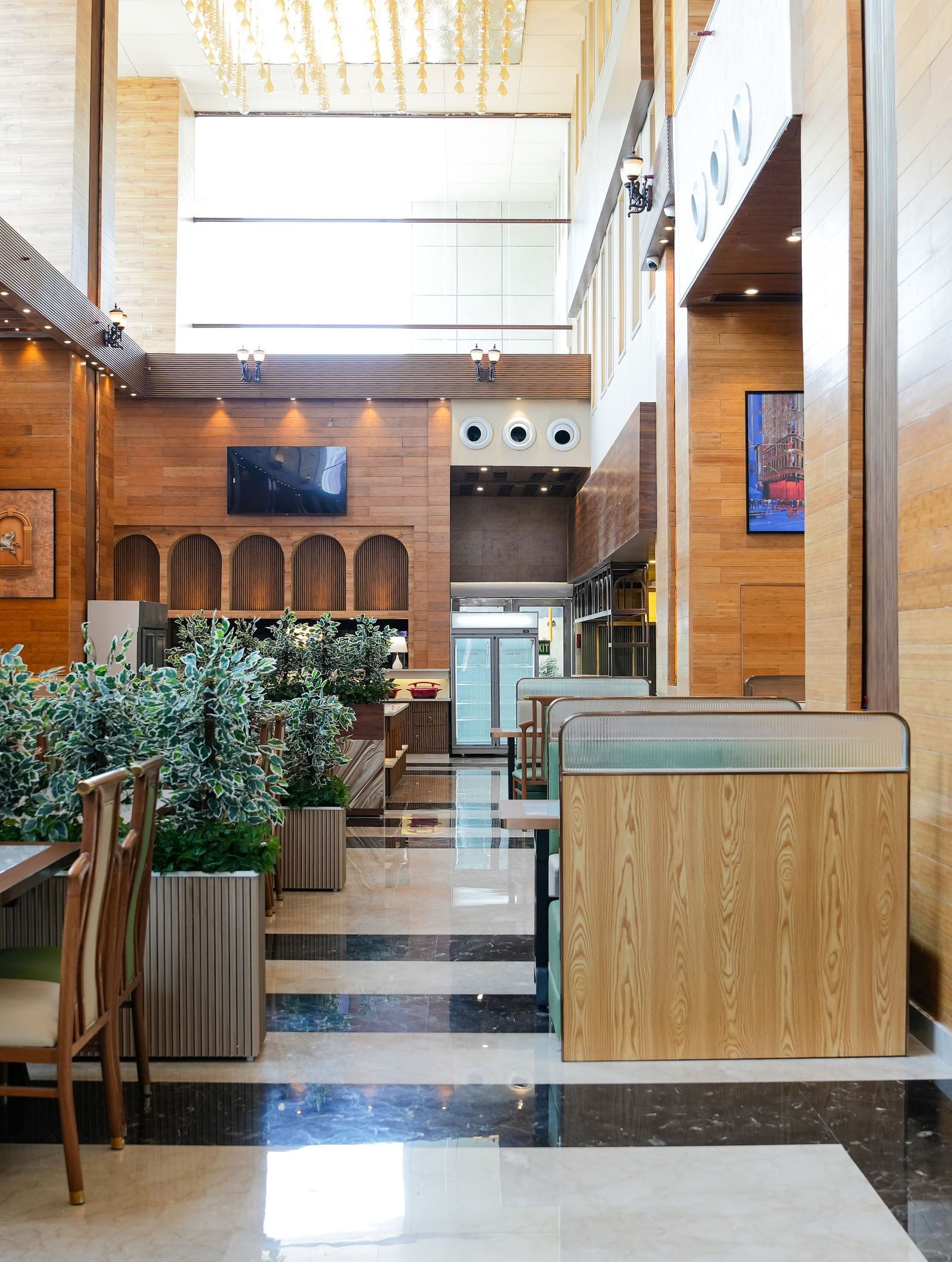 A bright and inviting dining area at The Meriton, adorned with lush green plants, comfortable booth seating in light green, and wooden wall accents.